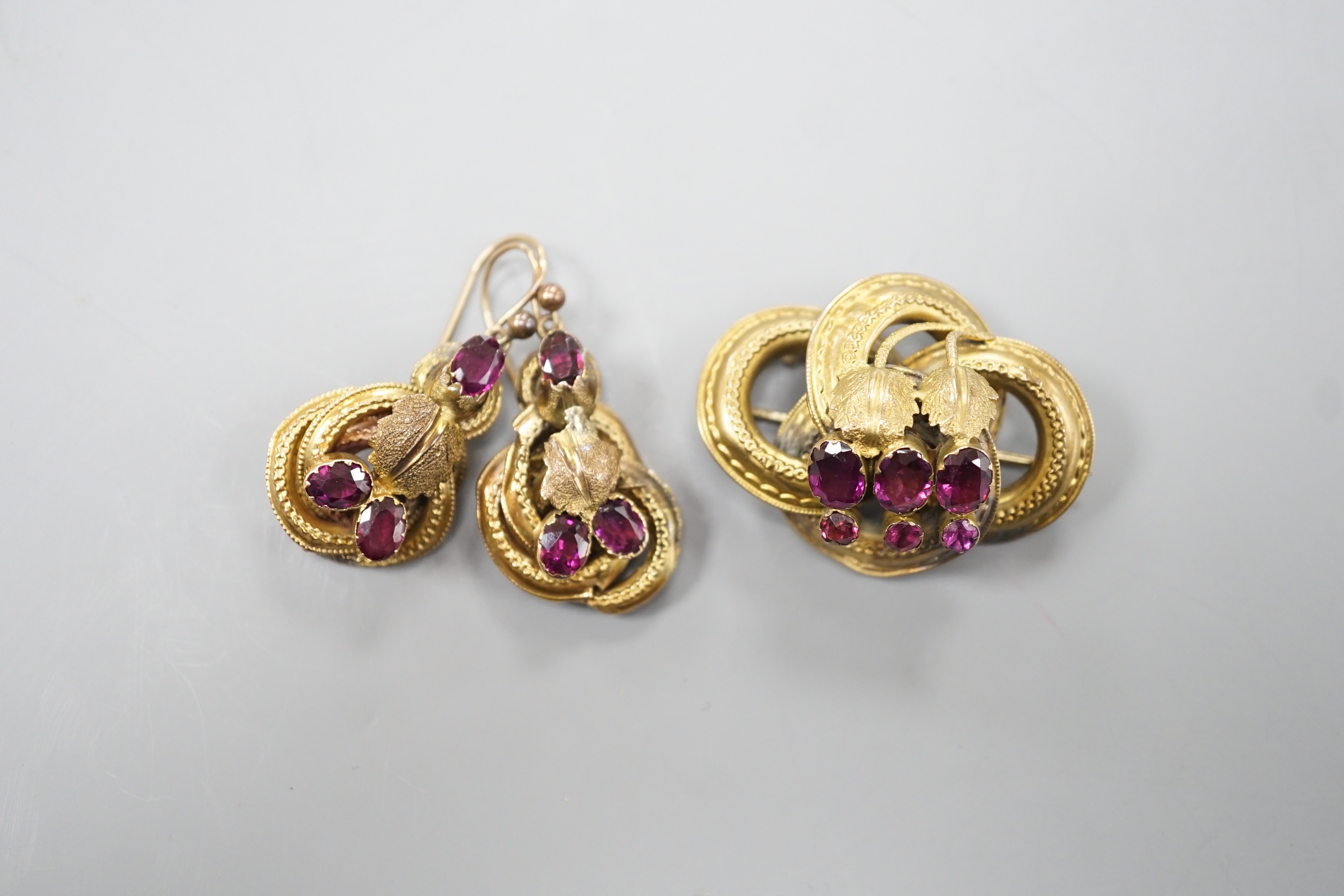 A Victorian yellow metal, oval and round cut garnet set demi parure, comprising a scroll work brooch and pair of matching earrings(a.f.), brooch, 38mm, gross weight 14 grams.